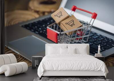 Mini shopping cart with boxes on laptop keyboard symbolizes e commerce, wooden surface below Wall mural