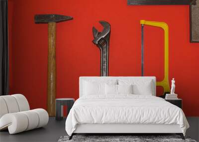 Metal hammer, wrench, and saw on red background Wall mural