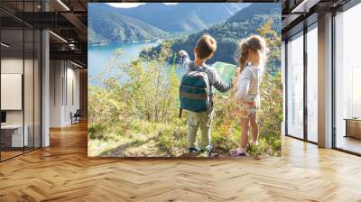 A cool independent boy scout with a tourist backpack and map shows his blond sister Ledro Lake, which they discovered while traveling around the mountain lake in the Alps. Wall mural