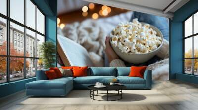 Cozy home setting, a person reading a book with a bowl of popcorn by their side, emphasizing relaxation and comfort on National Popcorn Day Wall mural