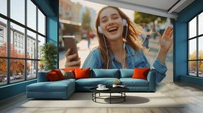 Happy young woman in earphones is listening to music with smart phone, dancing and smiling Wall mural