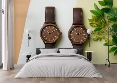 Top view of two brown wooden watches set against a white and brown backdrop. Green foliage and a leather band watch on a softly colored background Wall mural