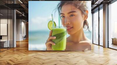 Woman drinking vegetable Green detox smoothie after fitness running workout on summer day. Fitness and healthy lifestyle concept with beautiful fit mixed race Asian Caucasian model outside on beach. Wall mural