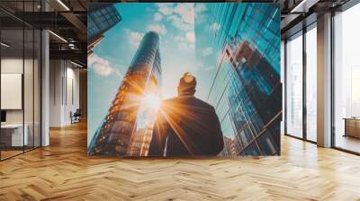 A man stands in front of a tall building with a bright sun shining on him Wall mural