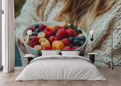 A woman is holding a bowl of fruit, including raspberries and blueberries. Concept of freshness and health Wall mural