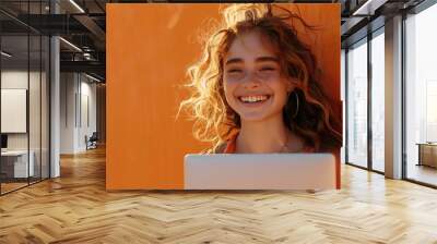 A woman with curly hair is smiling and holding a laptop Wall mural