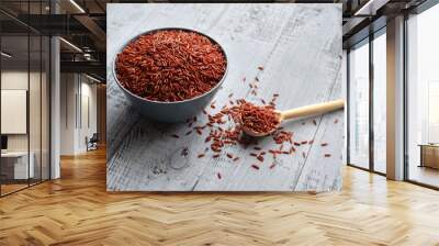 Bowl and full spoon with uncooked red rice on wooden background Wall mural