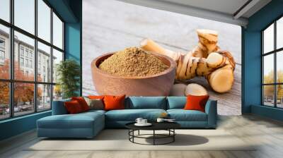 Alpinia galanga powder in wooden bowl and fresh galangal rhizome  isolated on wooden table background.  Wall mural