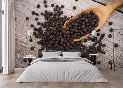 Black pepper seeds or peppercorns ( dried seeds of piper nigrum) in wooden spoon isolated on wood table background. top view. Flat lay. Wall mural