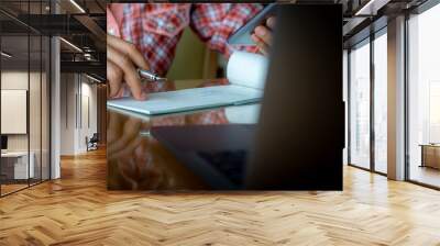 Business person hand using mobile smart phone and writing and signing cheque book,work on laptop computer at workplace. Wall mural