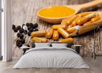 Curcuma capsules and Curcumin powderin wooden spoon and black peppercorns isolated on rustic wood table background. Health benefits and antioxidant food concept. Wall mural