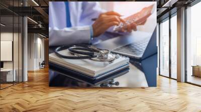 Female doctor or practitioner using calculator and work on laptop computer with medical stethoscope  and notebookon the desk at clinic or hospital. Medical healthcare costs ,fees and revenue concept. Wall mural