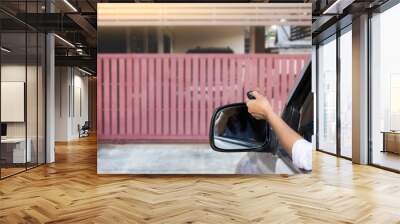 Woman in car, hand using remote control to open auto wooden door with modern home blurred background. Automatic gate concept.	 Wall mural