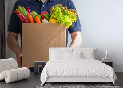 Food delivery service - man with a cardboard box of fresh vegetables on a gray background. Copy space Wall mural