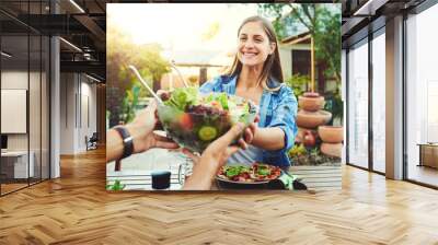 Always try to make every meal a healthy one. young woman taking a salad bowl from a friend while sitting around a table outdoors. Wall mural