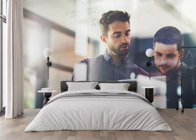 Working on their top ideas to expand their company. Shot of two young businessmen using a digital tablet while brainstorming on a glass wall in an office. Wall mural