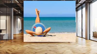 A slender girl on the beach in a straw hat in the colors of the Aruba flag. The concept of a perfect vacation in a resort in the Aruba. Focus on the hat. Wall mural