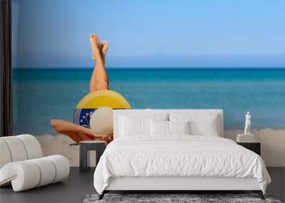 A slender girl on the beach in a straw hat in the colors of the Venezuelan flag. The concept of a perfect vacation in a resort in the Venezuela. Focus on the hat. Wall mural