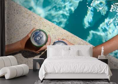 Two hands hold cans of cold drink in the pool on a hot day. The concept of vacation in a friendly company. Top view, selective focus on the bank. Wall mural