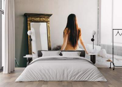 beautiful brunette woman in dress standing near big mirror in bedroom and looking on herself, fittin Wall mural