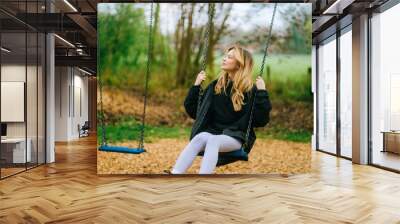 Joyful and youthful woman on a swing at the park. Concept pf people and no limit age to play and have fun. Female in outdoors leisure activity using swing and enjoy life Wall mural