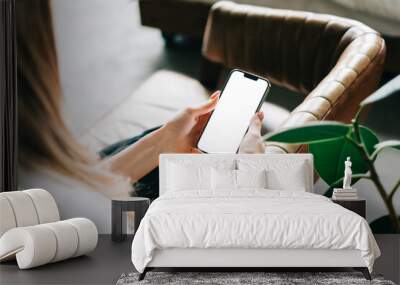 Woman holding mobile phone with white screen mock up, resting on a sofa in living room at home.	 Wall mural