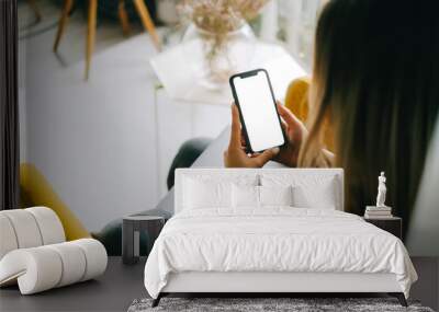 Woman holding mobile phone with white screen mock up, resting on a sofa in living room at home. Wall mural