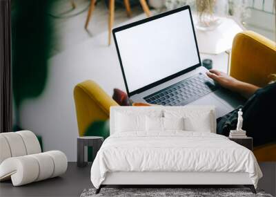 Young caucasian woman sitting on sofa at home and using laptop computer with white blank screen, mock-up. Wall mural