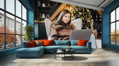 Young caucasian woman using laptop computer in holidays at home in the armchair in living room. Wall mural