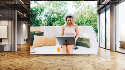 Young caucasian woman using laptop computer outdoor, sitting on a bench in the backyard in summer day. Wall mural