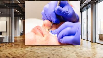 Beautician using a mechanical tool with a spoon to remove uno and clean acne on the patient's face in a beauty salon, facial care. Wall mural