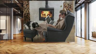 Beautiful middle-aged woman next to the fireplace relaxes in the living room and works on laptop from house. Girl in 30's surveyed for the  home bussiness project Wall mural