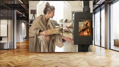 Beautiful young woman in middle age in  living room covered with blanket  drinks tea from a blue bowl in the afternoon at the fireplace with fire. Winter time Wall mural