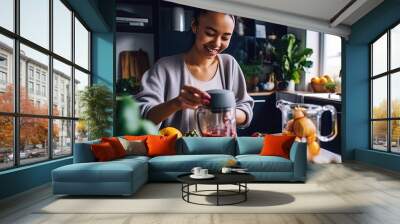 Mixed ethnicity young woman preparing a healthy smoothie at home in the kitchen Wall mural