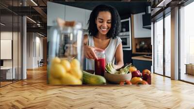 Young woman using fruits and vegetables to make a healthy smoothie in the kitchen  Wall mural