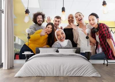 team of successful multiethnic coworkers taking selfie at modern office workplace. all happy, smiling and waving at camera Wall mural