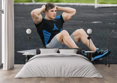 Fitness man doing sit ups in the stadium, working out. Active male exercising abdominals Wall mural