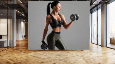 Fitness woman doing exercise for biceps on gray background. Muscular woman workout with dumbbells Wall mural