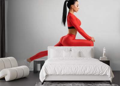 Fitness woman doing lunges exercises for leg muscle workout training. Active girl doing front forward one leg step lunge exercise, on the gray background Wall mural