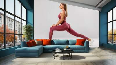 Fitness woman doing lunges exercises for leg muscle workout training. Active girl doing front forward one leg step lunge exercise, on the gray background Wall mural