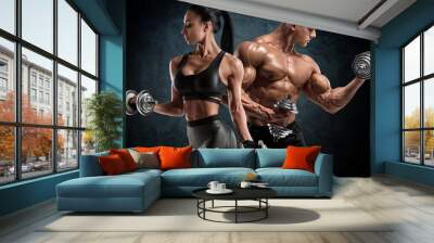 Sporty couple workout with dumbbells. Muscular man and woman showing muscles Wall mural