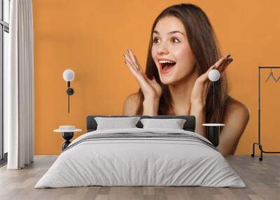 Surprised happy beautiful woman looking sideways in excitement. Isolated on orange background Wall mural