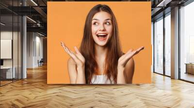 surprised happy beautiful woman looking sideways in excitement. isolated on orange background Wall mural