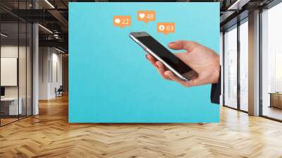 Female hand holding phone, surrounded with social media icons on blue background. Social media concept Wall mural