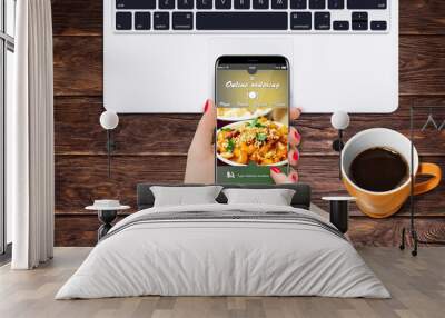 Girl at home ordering vegetarian food while sitting at desk in front of laptop and coffee Wall mural