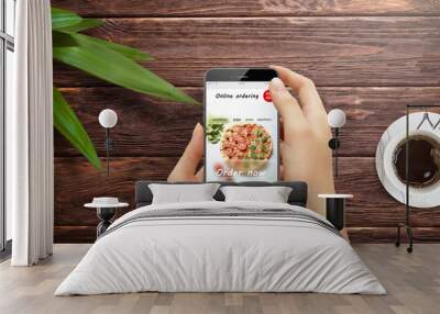 Girl ordering pizza online on smartphone, with table and coffee and plant in background Wall mural