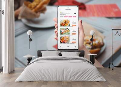 Woman in the restaurant ordering food with app on her phone, blurred table with food in background Wall mural