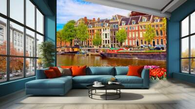 Cityscape view of the canal of Amsterdam in summer with a blue sky and traditional old houses. Colorful spring tulips flowerbed on the foreground. Picturesque of Amsterdam, The Netherlands. Wall mural