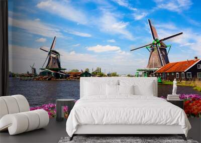 Dutch typical landscape. Traditional old dutch windmills with house, blue sky near river with tulips flowers flowerbed in the Zaanse Schans village, Netherlands. Famous tourism place. Wall mural