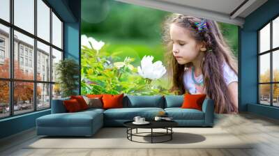 Little girl looking into the flower in green garden or park. Wall mural